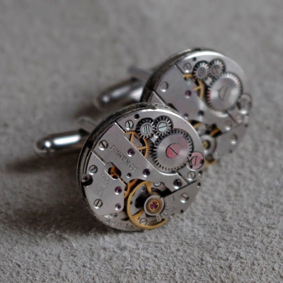 A pair of silver cufflinks made from vintage watch mechanisms, featuring intricate gears and jewels.